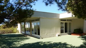 Un edificio moderno con ventanas amplias y techo plano, rodeado de árboles y vegetación.