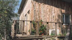 Un edificio rústico de madera con base de piedra, una terraza de madera y plantas en macetas.