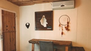 Una habitación con escritorio de madera, una silla, un atrapasueños y un aire acondicionado de pared.