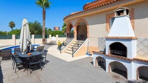 Una terrazza esterna con piscina, barbecue e tavolo con sedie.