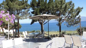 An outdoor patio with tables and chairs, a pergola with an umbrella, and a view of the sea. - Seafront apartment for 4 people in the heart of nature (CALCATOGGIO)