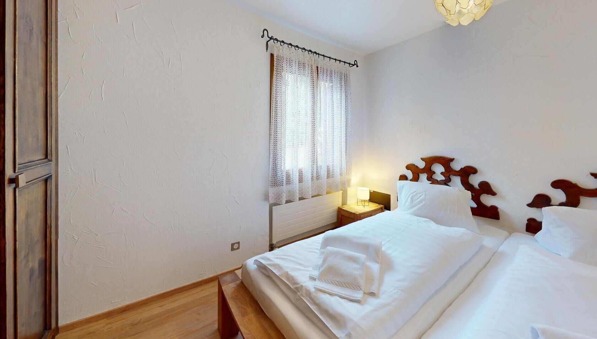A neatly made bed with white linens, a wooden headboard, and a bedside table with a lamp.