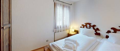 A neatly made bed with white linens, a wooden headboard, and a bedside table with a lamp.
