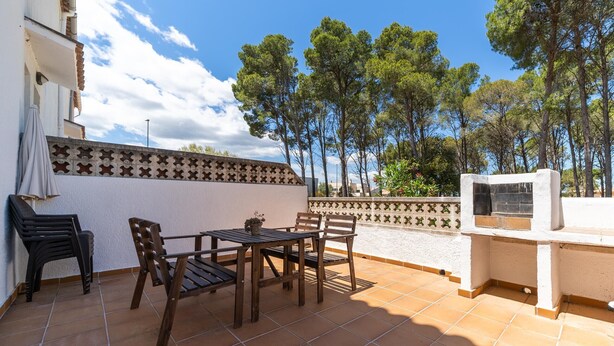 A patio with a table and chairs, a barbecue grill, and a view of trees.