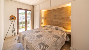 A bedroom with a large bed, a wooden headboard, a floor lamp, and a view of the outside through a sliding door. - Gardernia: House for holiday rental with community garden and pool (L'Escala)