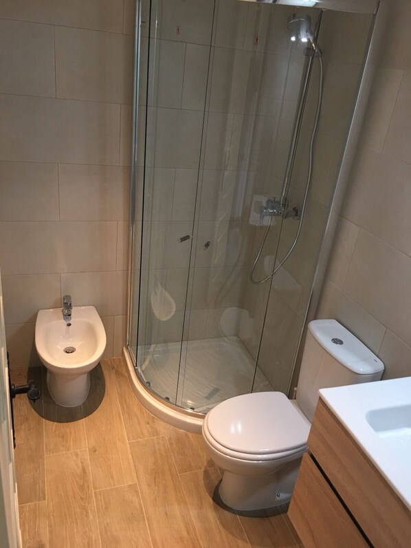 Een badkamer met een douchecabine, een wastafel met voetpedaal en een toilet.