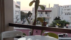 A balcony with a round table and two chairs, overlooking a cityscape with buildings and a clear sky. - Es Pujol: Apartment/ flat - Es Pujol (Es Pujol)