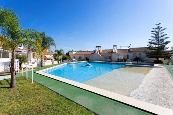 Une piscine rectangulaire avec une fontaine au centre, entourée d’une pelouse verdoyante et d’une terrasse en pierre.