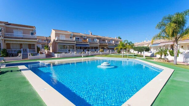 A swimming pool with a fountain, surrounded by multi-story buildings with balconies and a clear blue sky. - CH Ronda Doña Pepa (Ciudad Quesada) (Ciudad Quesada)