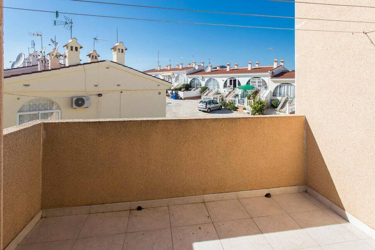 Un balcón con vista a edificios cercanos y un coche estacionado.