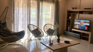 Ein modernes Wohnzimmer mit einer Couch, zwei Sesseln, einem Couchtisch, einem Fernseher und einem Bücherregal.