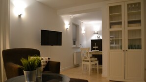 Uma sala de estar com televisão de tela plana na parede, uma mesa de jantar com cadeiras e um armário com portas de vidro.