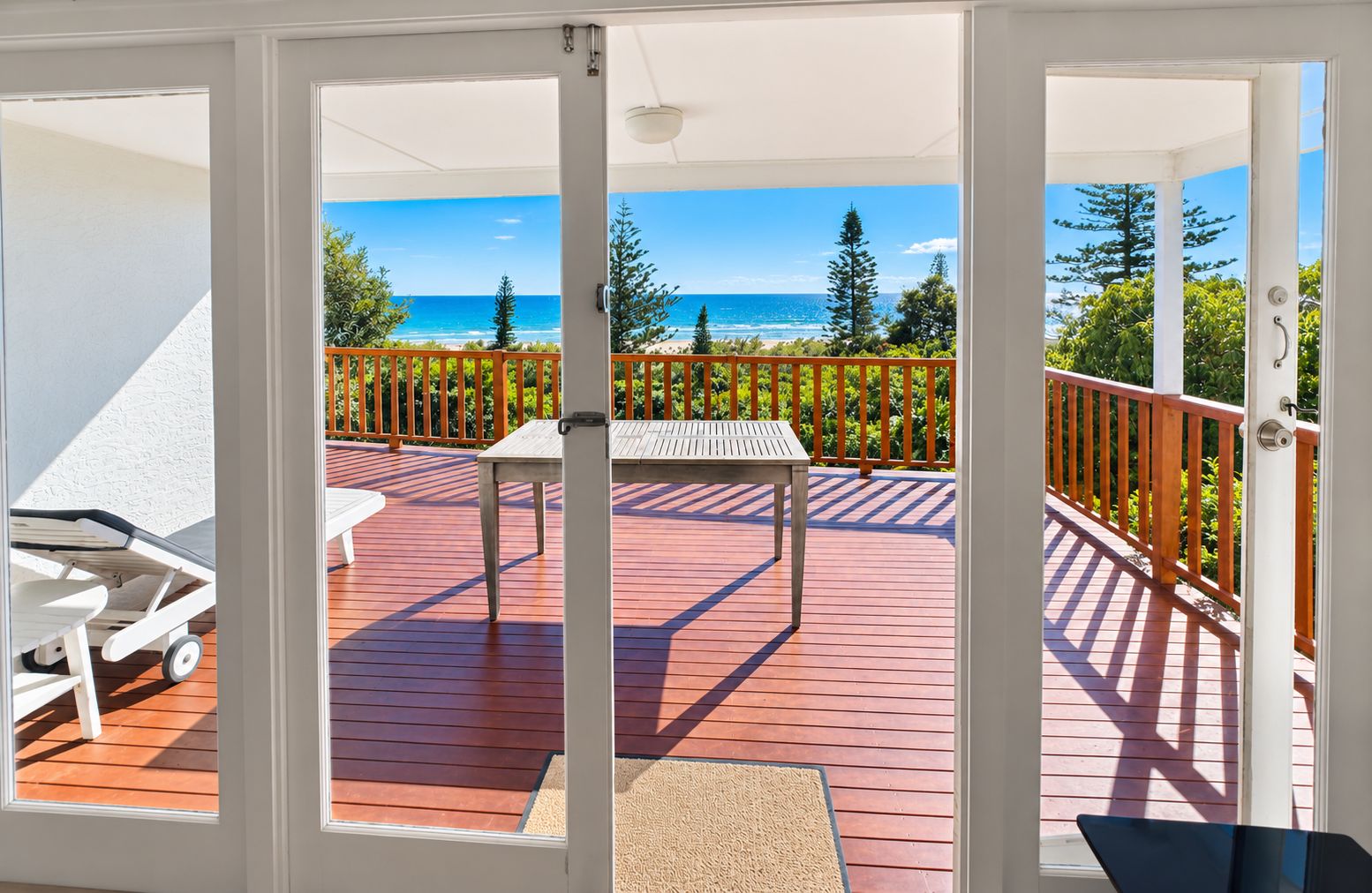 A deck with a table and chairs, overlooking a beach and trees.