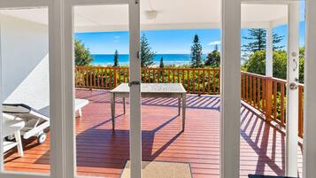 A deck with a table and chairs, overlooking a beach and trees.