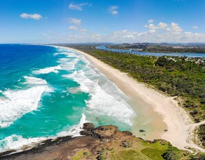 A coastal landscape with a beach, ocean, and distant hills.