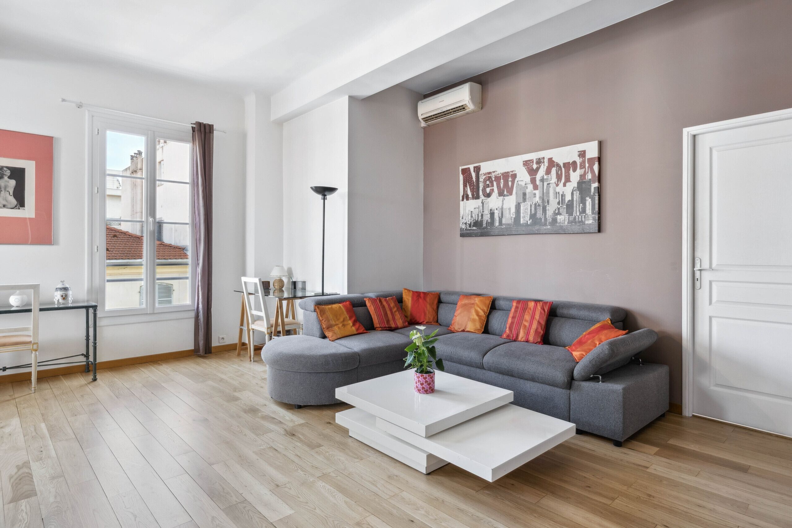 A modern living room with a grey sectional sofa, a white coffee table, and a cityscape poster on the wall.