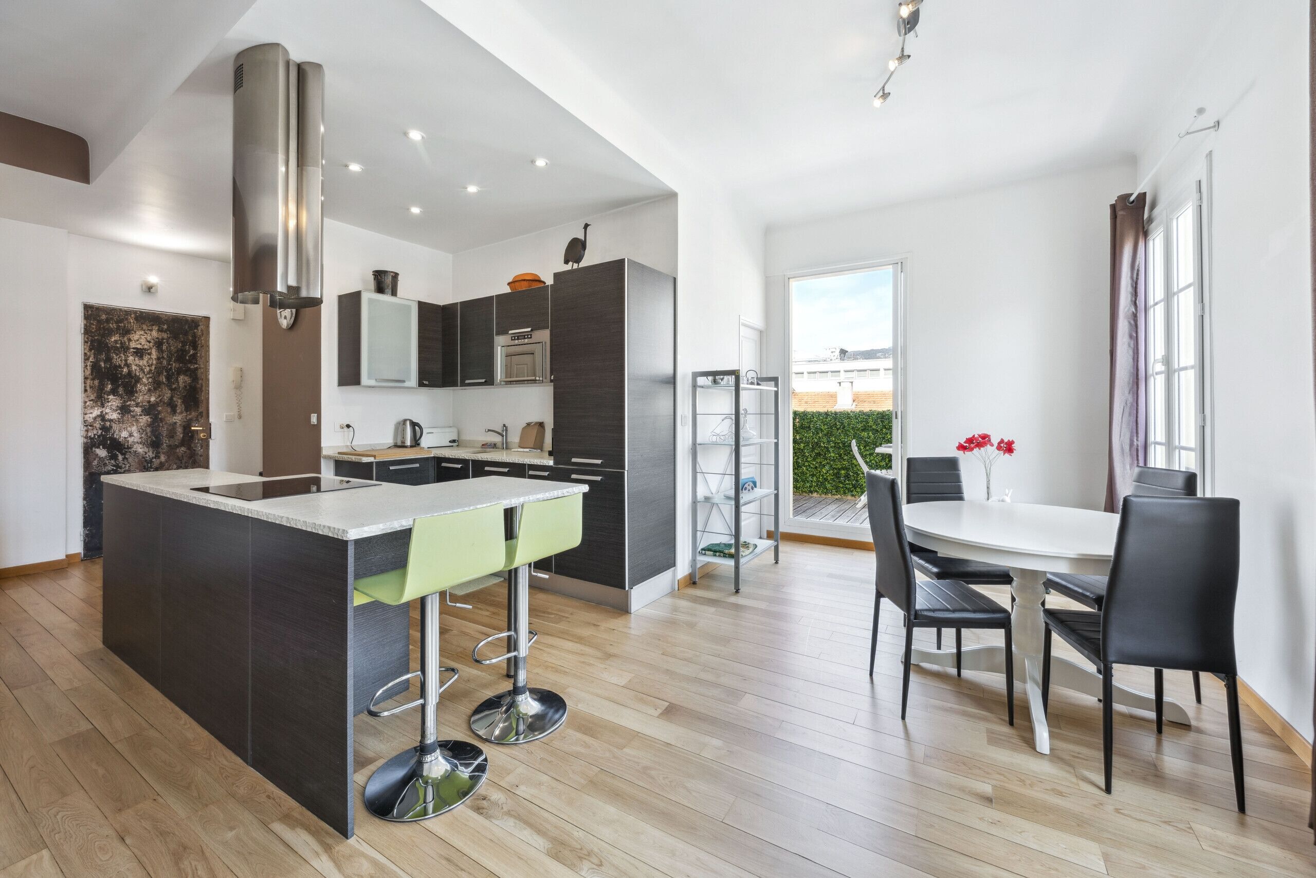 A modern kitchen with a central island, bar stools, and a dining area with a table and chairs.