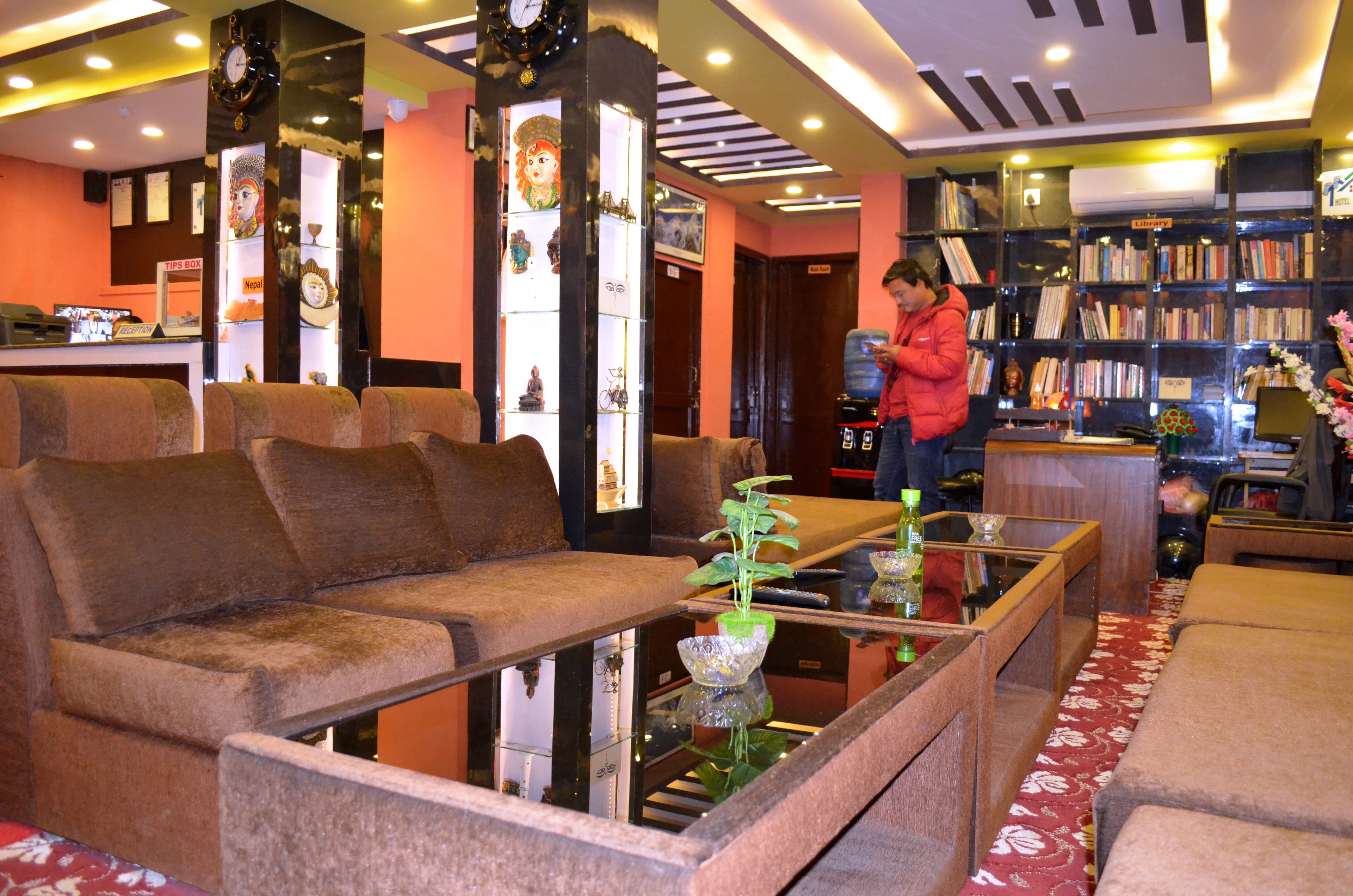 A lobby with a sofa, a glass coffee table with a plant, and a bookshelf filled with books.