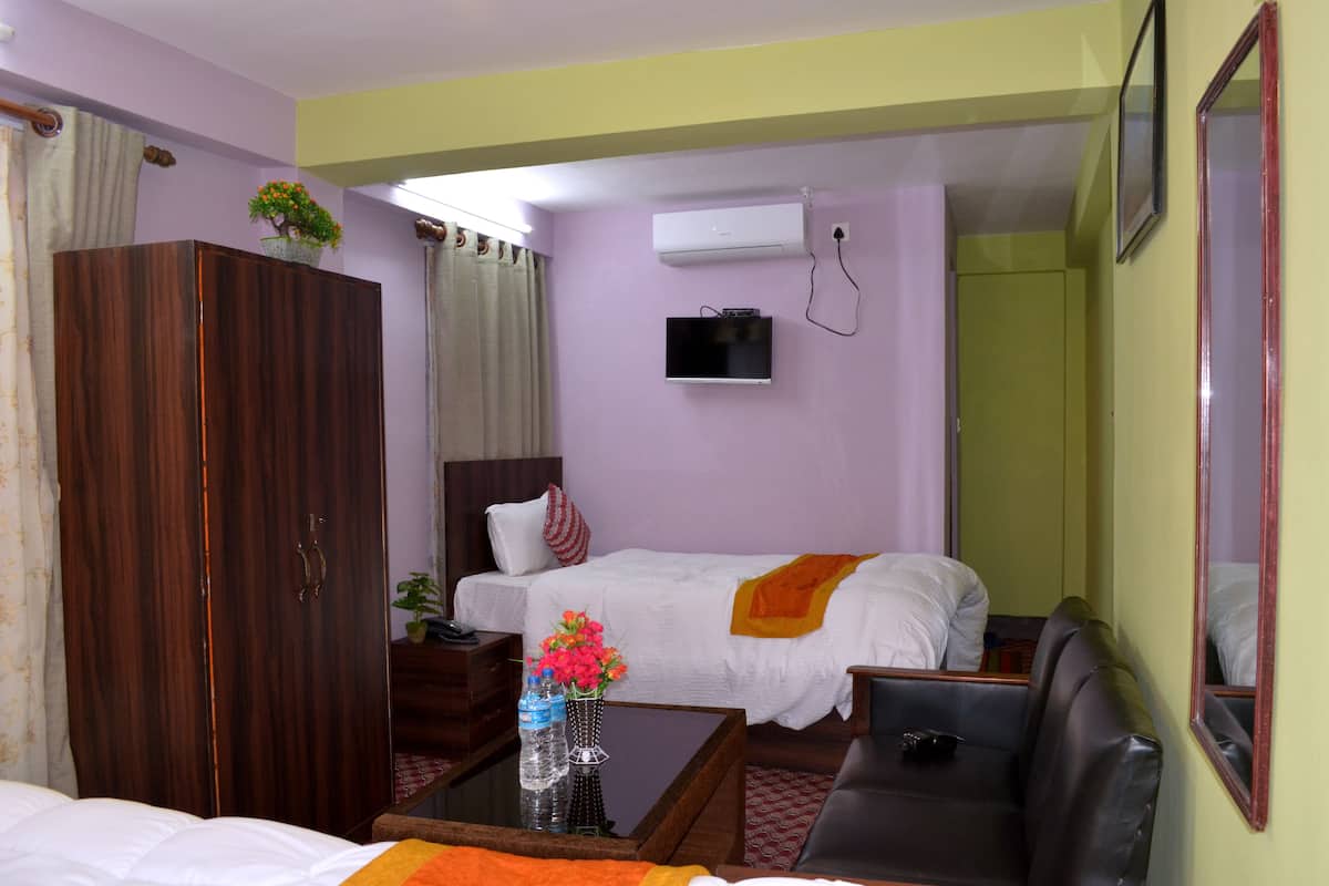 A hotel room with a wooden wardrobe, a bed with white bedding, a television mounted on the wall, a sofa, and a small table with a vase of flowers.