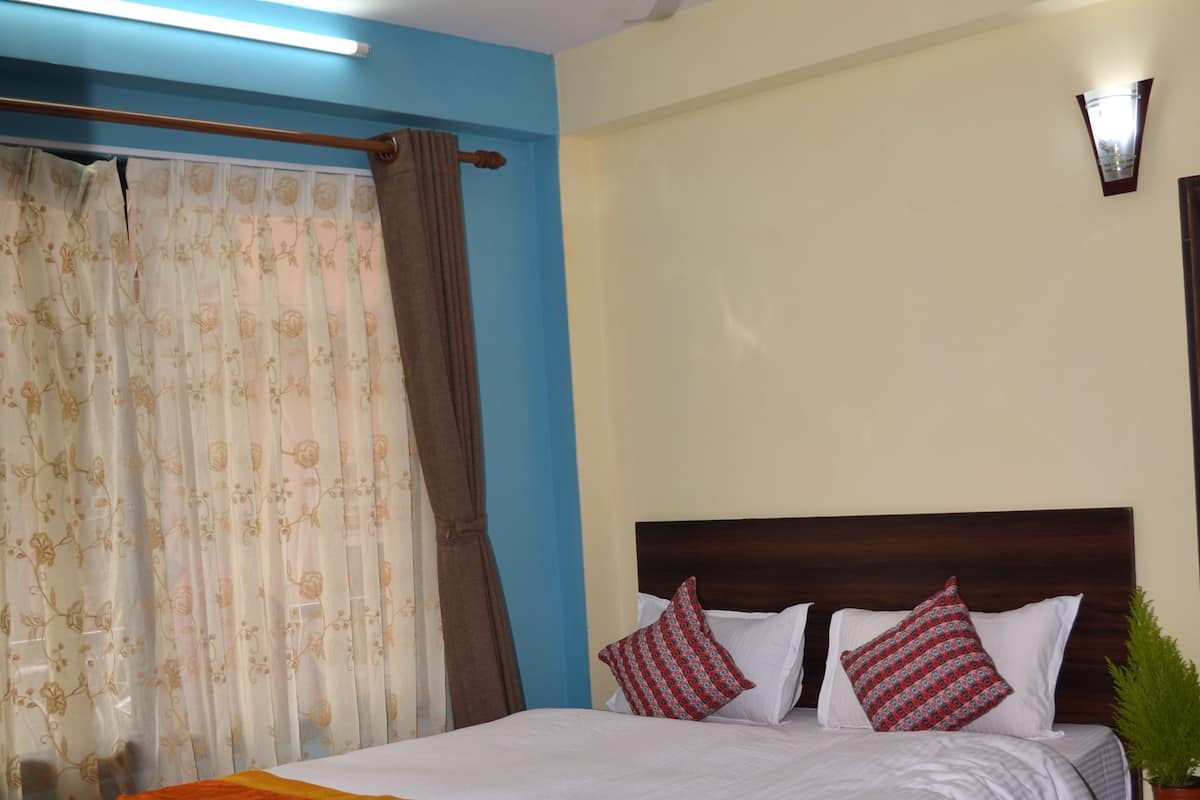 A hotel room with a bed, a ceiling fan, curtains, a nightstand, and a potted plant.
