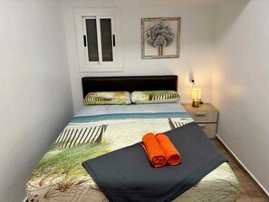 A bedroom with a bed, pillows, a nightstand, a lamp, and a framed picture on the wall.