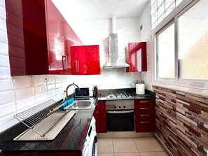 A kitchen with red cabinets, a stainless steel range hood, a gas stove, a built-in oven, and a window.