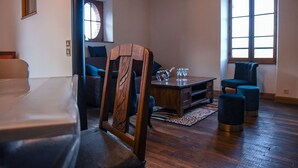 Een gezellige woonkamer met een houten salontafel, twee fauteuils, een bank en een groot raam dat natuurlijk licht binnenlaat.