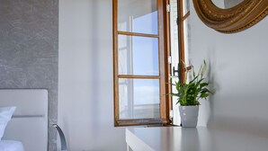 Een slaapkamer met een bed, nachtkastje, een potplant, raam en spiegel.