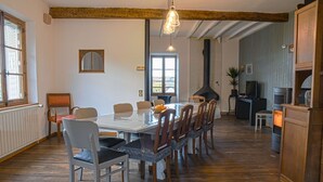Een eetruimte met een lange houten tafel en stoelen, een groot raam en een stenen openhaard.