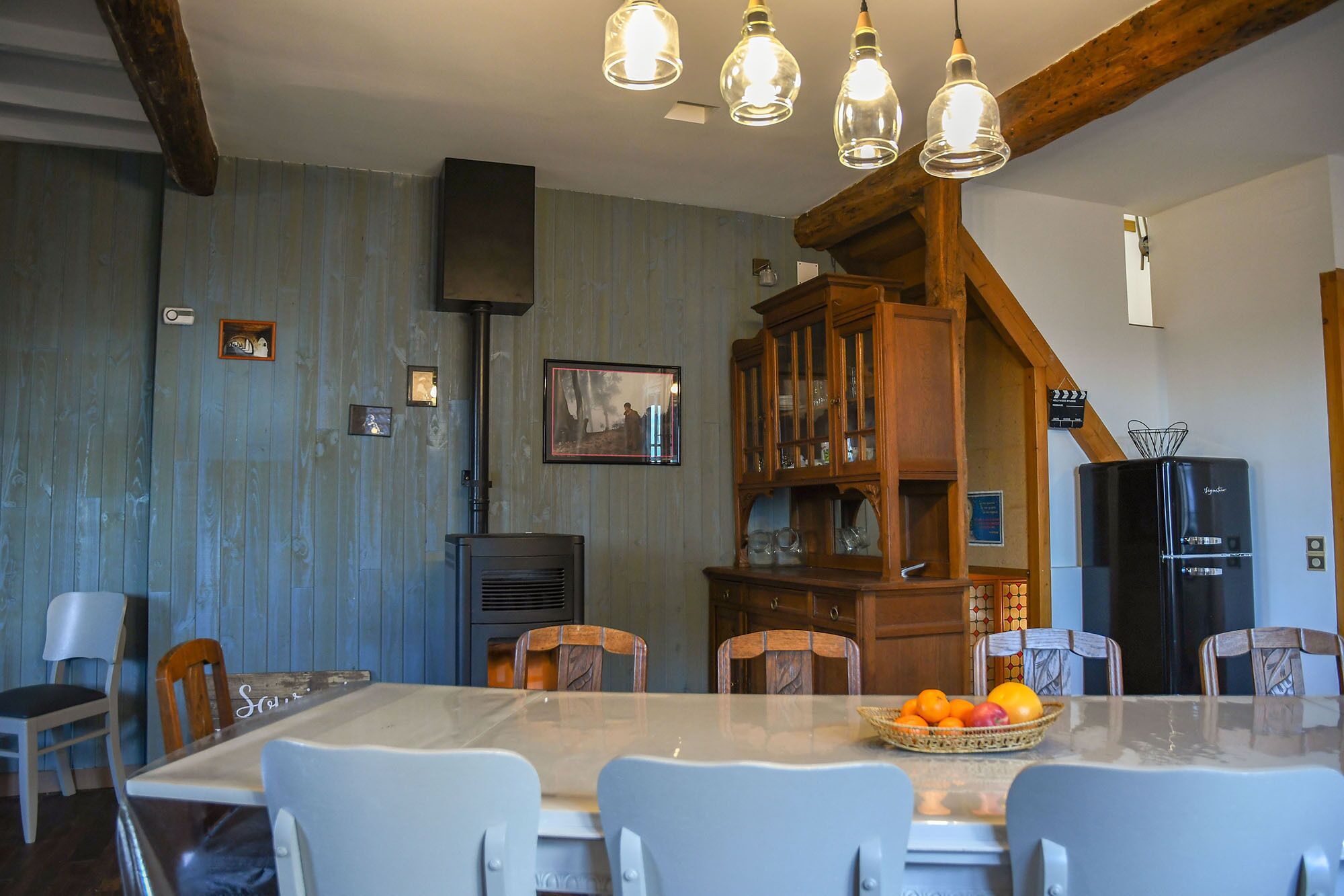 Un comedor con una mesa de vidrio, sillas blancas, un armario de madera y un refrigerador negro.