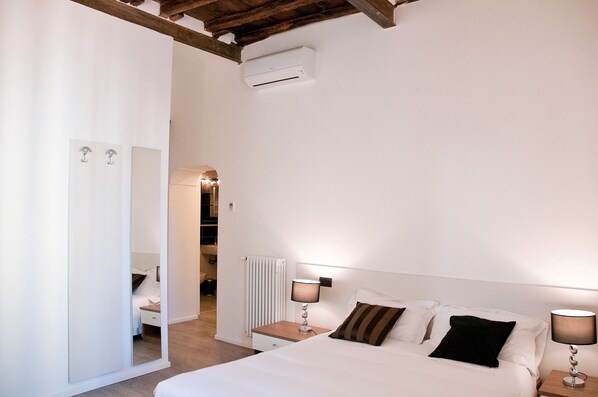 A bedroom with a bed, bedside lamps, a mirror, and a radiator.