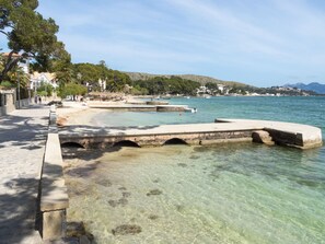 A coastal walkway with clear water, a stone bridge, and a beach area.