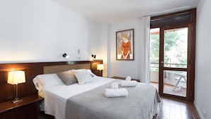 Een hotelkamer met een groot bed, twee bedlampen, een schilderij aan de muur en een balkon met een tafel en stoelen.
