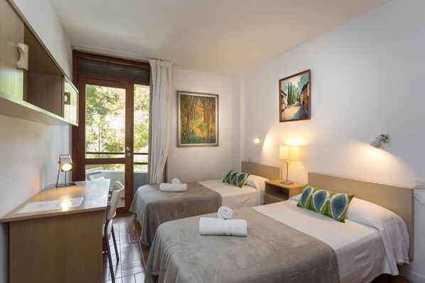 A hotel room with two beds, a desk, a chair, a window with curtains, and a painting on the wall.