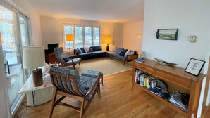 Amplia sala de estar con suelo de madera, un sofá, una silla, una estantería y un televisor.