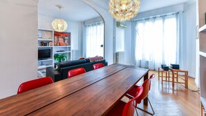 Un comedor moderno con una mesa de madera y sillas rojas, una sala de estar con sofá y televisor, y una lámpara decorativa de gran tamaño.