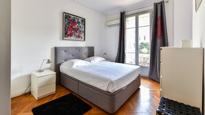 Un dormitorio con cama, mesita de noche, lámpara, cómoda y ventana con cortinas.
