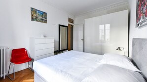 Un dormitorio con una cama grande, una silla roja, un aparador y un armario.