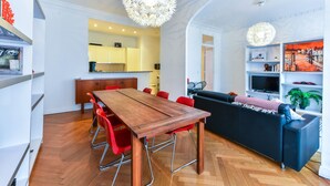 Una sala moderna con una mesa de comedor de madera, sillas rojas, un sofá negro y una lámpara de araña.