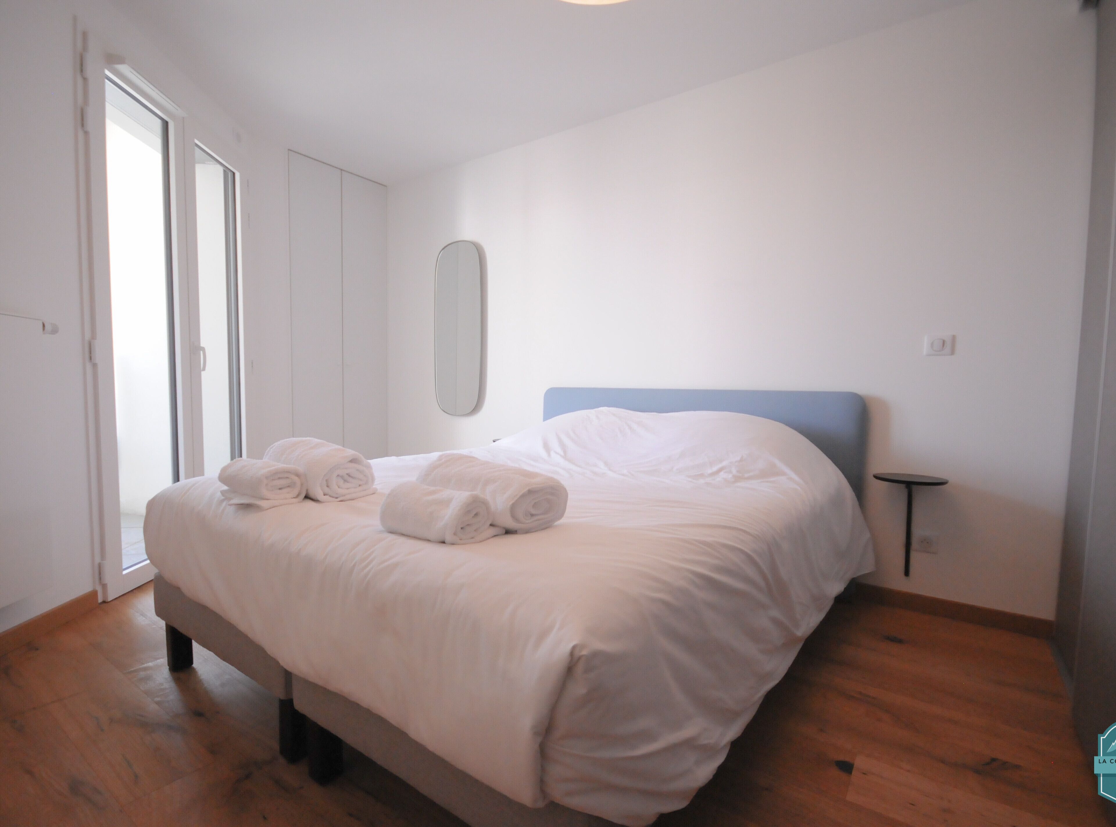 A neatly made bed with rolled towels, a small bedside table, and a mirror on the wall.