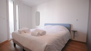 A neatly made bed with rolled towels, a small bedside table, and a mirror on the wall.