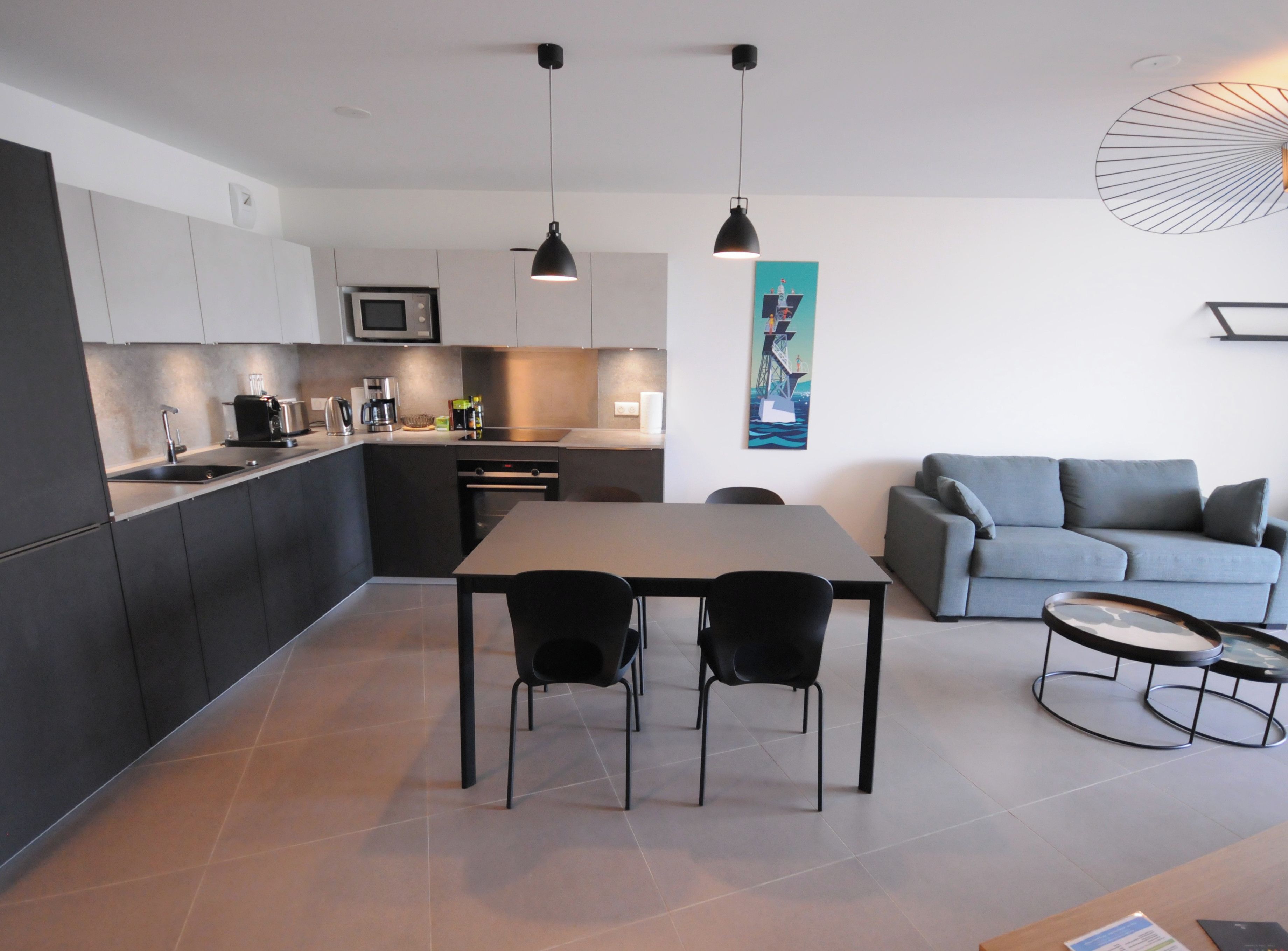 A modern kitchen with a dining area, a grey sofa, and a coffee table.