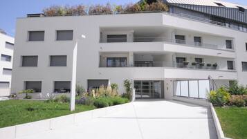 A modern multi-story building with a flat roof, balconies, and a central entrance.