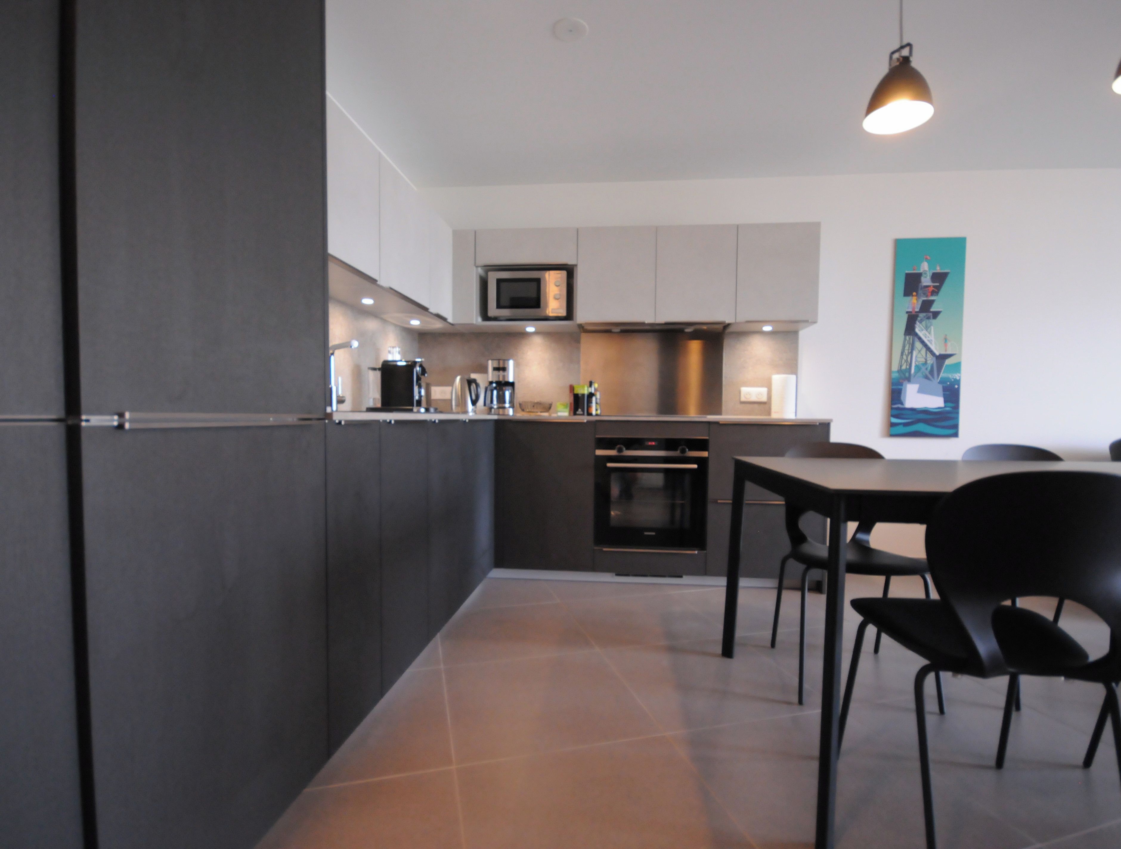 A modern kitchen with dark cabinetry, a microwave, oven, and a dining area with a table and chairs.