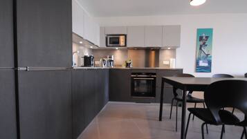 A modern kitchen with dark cabinetry, a microwave, oven, and a dining area with a table and chairs.