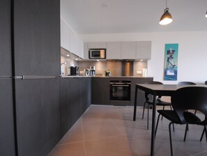 Una cocina moderna con armarios oscuros, microondas, horno y un comedor con mesa y sillas.