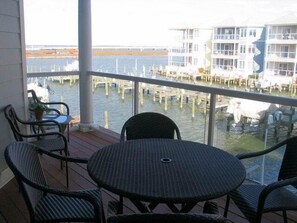Een balkon met rieten meubilair en uitzicht op een jachthaven met boten en gebouwen.