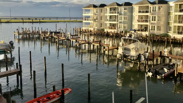 A marina with docked boats and a row of multi-story buildings with balconies. - Chincoteague Getaway on the Bay - Water Front,Pool ,IN TOWN ,LINENS & TOWELS (Chincoteague)