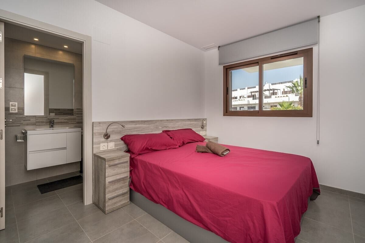 Un dormitorio con cama, ventana y baño con espejo y lavamanos.