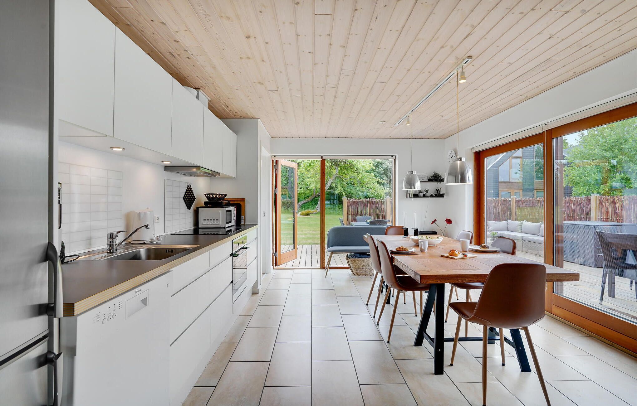 Et moderne køkken med et stort spiseområde, træloft og store vinduer.